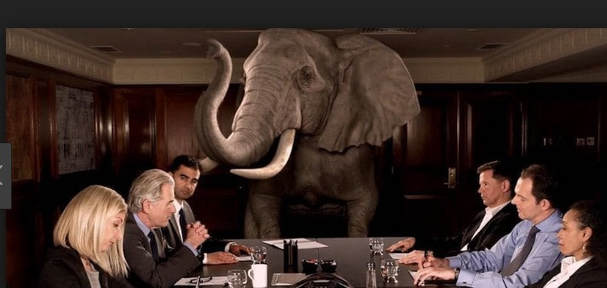 A photograph of a Brexit meeting, with a large elephant looming over the participants. The elephant in the room being the Irish/Northern Irish border