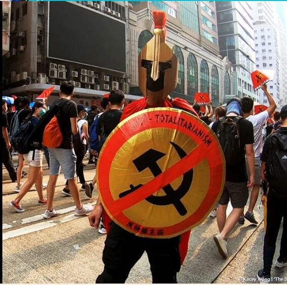 Artist Kacey Wong performing as a Roman soldier during a protest march, brandishing his shield 'Anti-Totalitarianism'. 