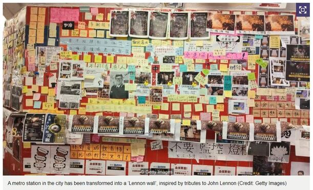 A large 'Lennon Wall' at a metro station in Hong Kong City, created by people putting up Post-It notes or other protest texts and images.