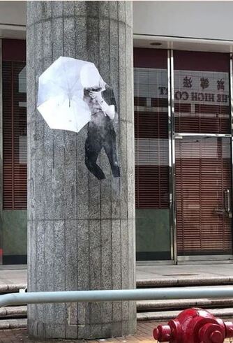 An image by Midnight Glue on a pillar showing a man with face concealed by a white umbrella, often used to hide the face and ward off tear gas.